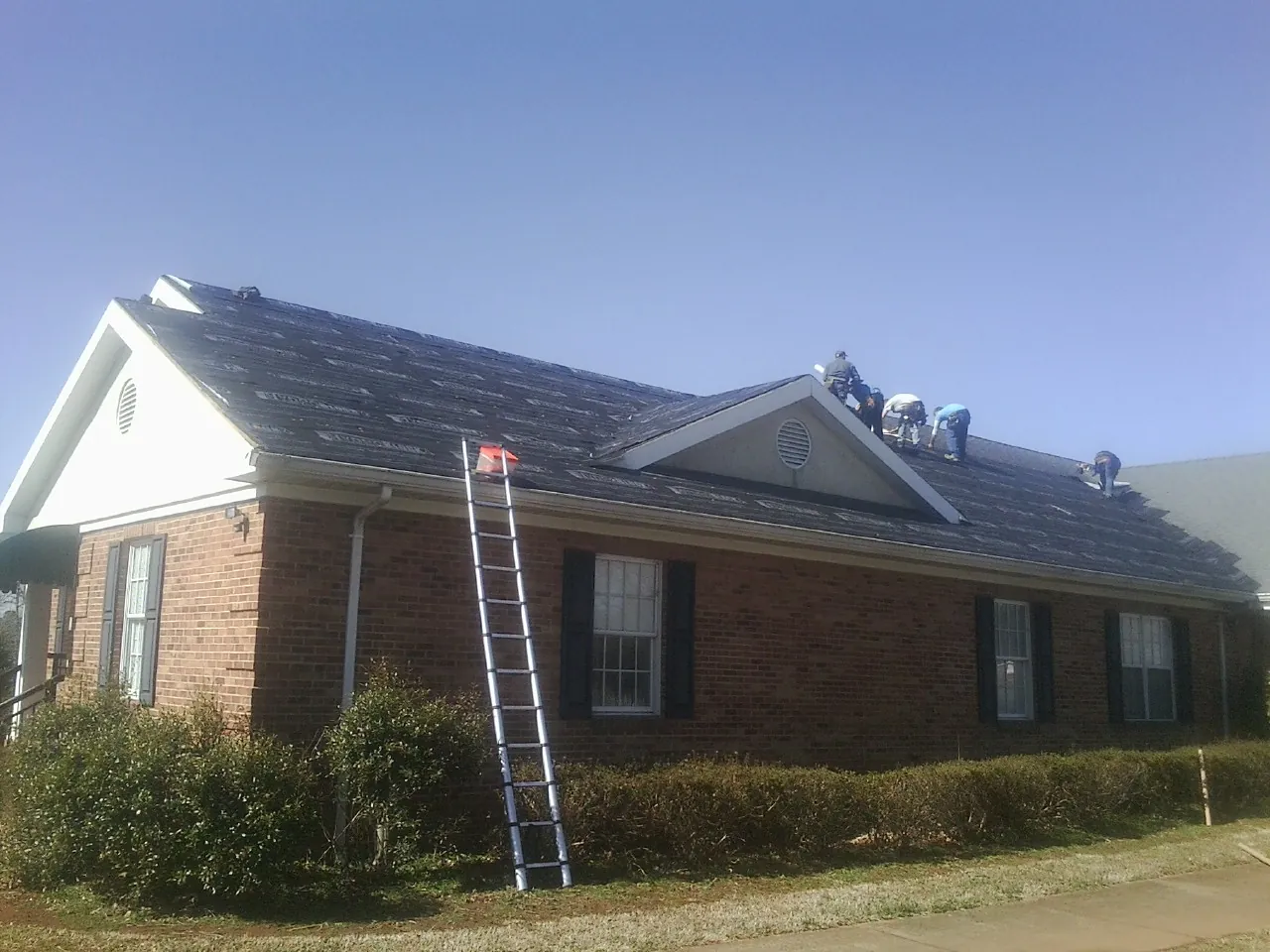 Crew tearing shingles off a brick ranch roof with a ladder set — Emergency Roof Repair work by our crew in Lottsburg