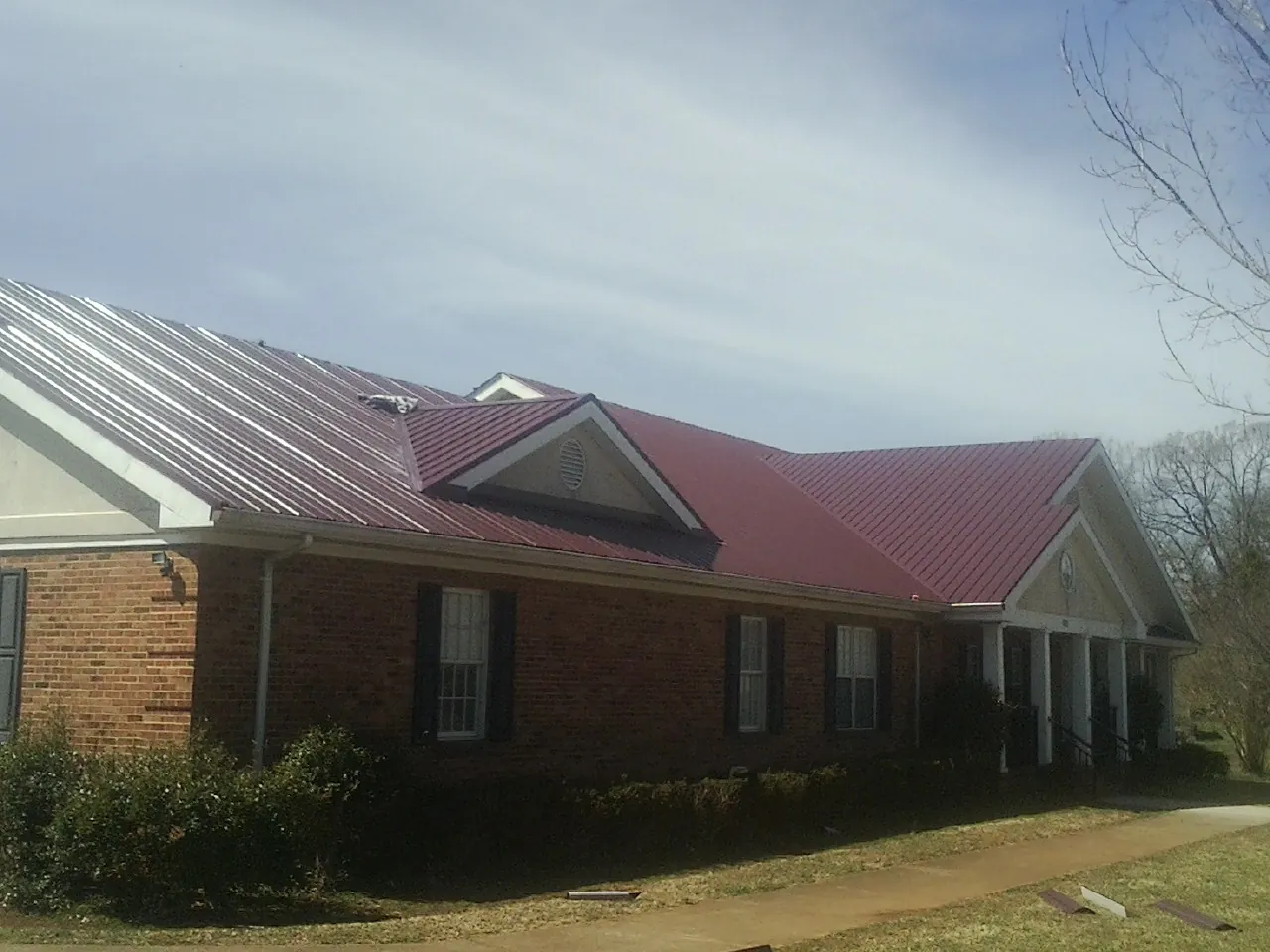 Red metal roof with gabled entries on a long brick building, from a Hail Damage Roof Repair job in Lottsburg