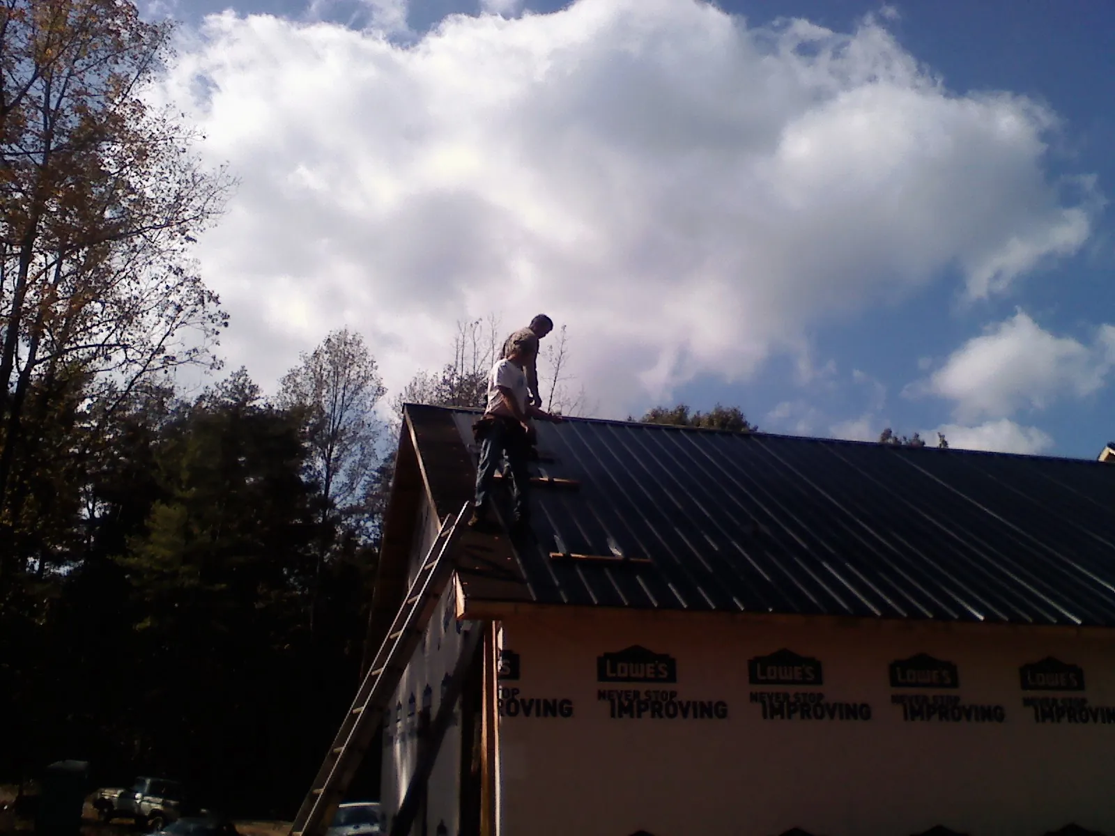 Roofer fastening dark metal panels high against a cloudy sky, from a Roof Inspection job in Lottsburg