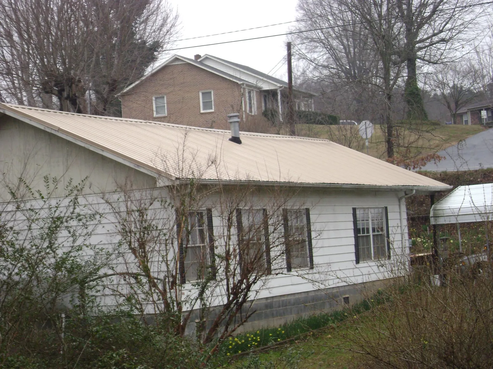 Tan metal roof on a white sided house set into a hillside — Commercial Roofing by Roofing Brothers in Lottsburg